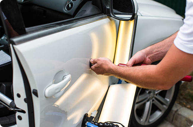 An automotive collision repair technician removes a dent from a car door panel.