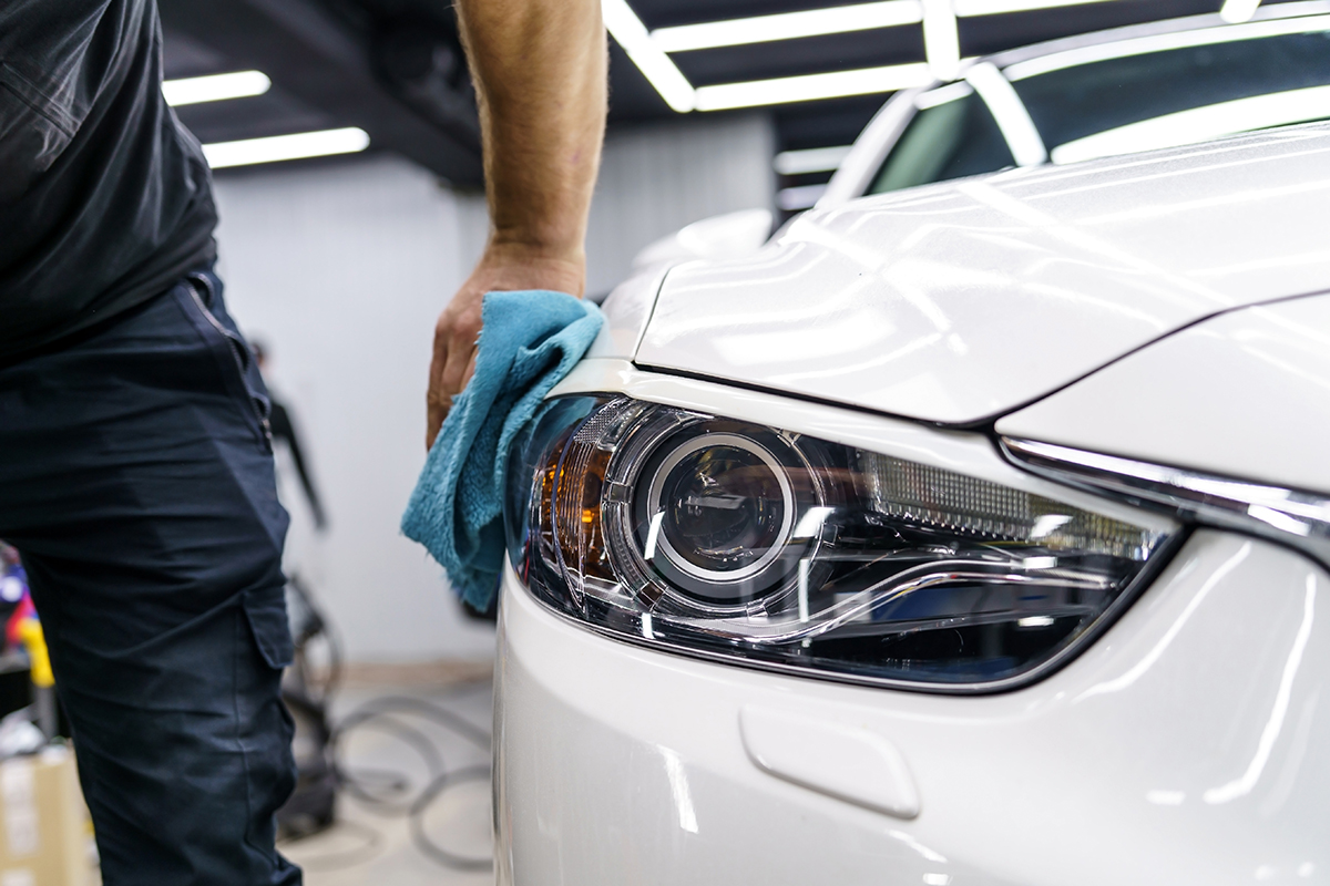 Paint repair technician buffs a white vehicle after removing a scratch