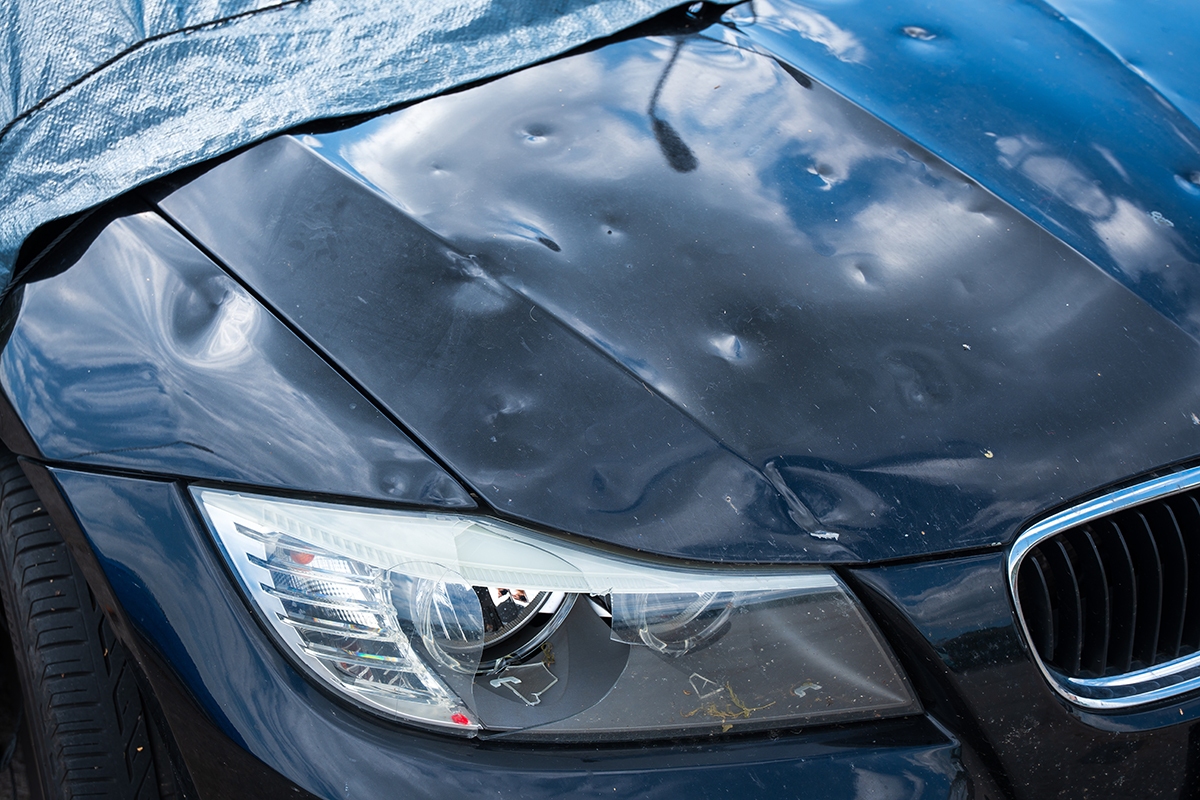 The hood of a BMW shows extensive pock marks from hail damage