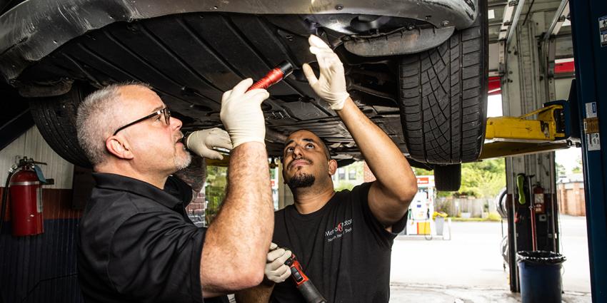 Two ASE-certified auto repair technicians inspect under a vehicle at Metro Motor