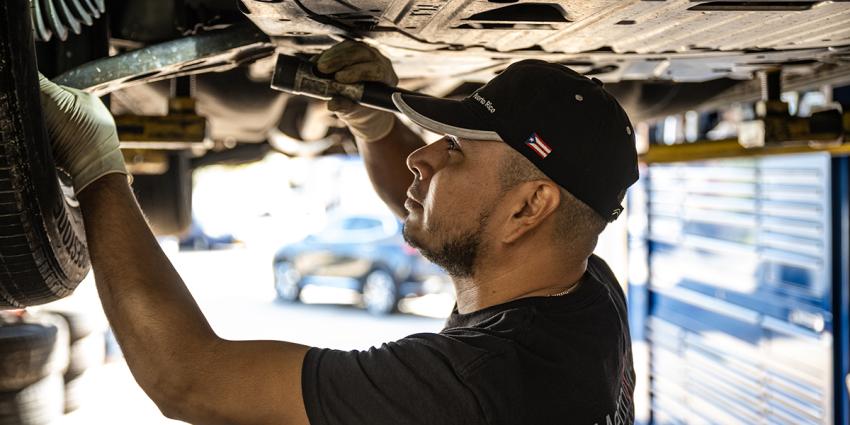 A vehicle technician inspects under a vehicle at a Metro Motor auto repair facility in Arlington, VA