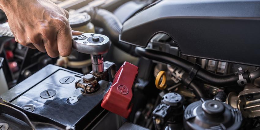 Auto repair technician inspects a vehicle's battery under the hood.