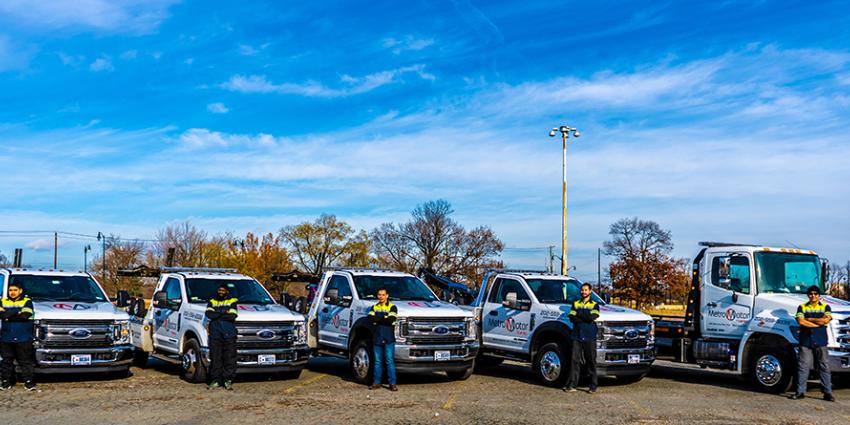 Metro Motor towing service operators stand in front of a row of tow trucks