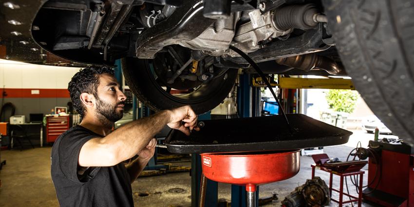 Auto repair technician drains oil from below a vehicle during an oil change service at Metro Motor