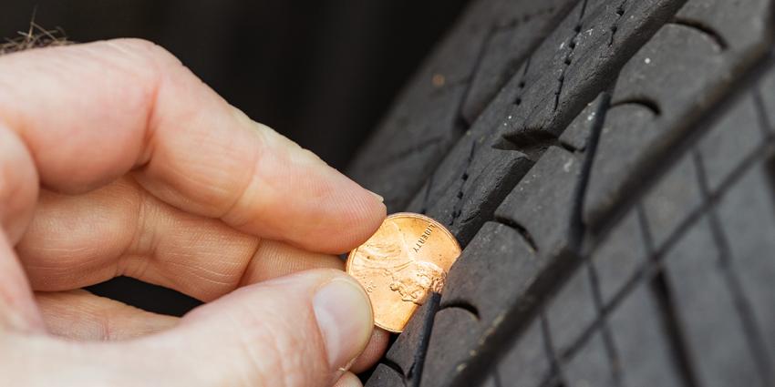 A man inserts a penny into treads to see if the tires need to be replaced.