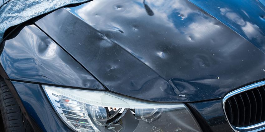 The hood of a BMW shows extensive pock marks from hail damage