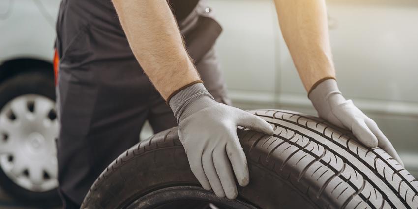 Auto repair technician rolls a single tire in an auto repair shop