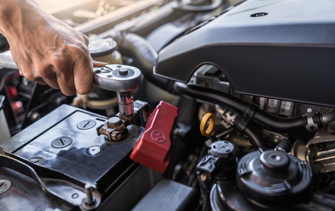 Auto repair technician inspects a vehicle's battery under the hood.