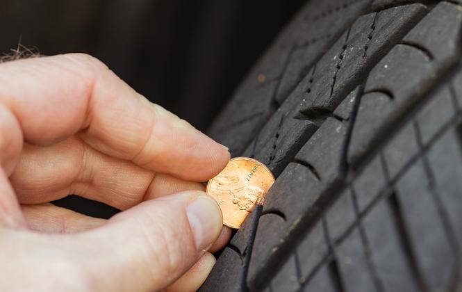 A man inserts a penny into treads to see if the tires need to be replaced.